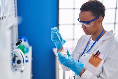 African american woman scientist pouring liquid on sample at laboratory