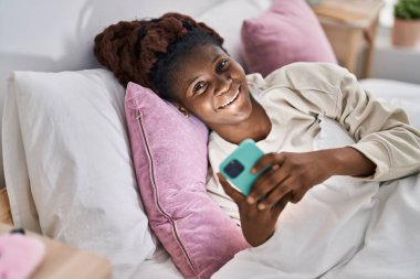 Afrika kökenli Amerikalı bir kadın yatakta akıllı telefon kullanıyor.