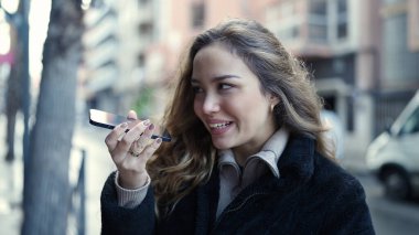 Young beautiful hispanic woman smiling confident sending voice message by smartphone at street