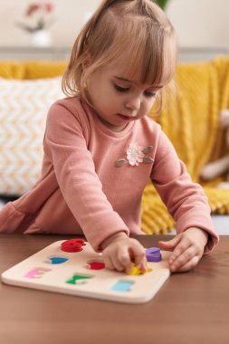 Adorable blonde girl playing maths puzzle game standing at home