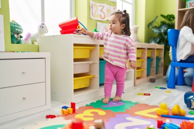 Adorable chinese toddler standing with relaxed expression at kindergarten
