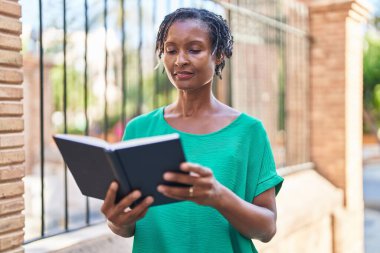 Middle age african american woman reading book at street