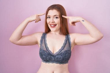 Redhead woman wearing lingerie over pink background smiling pointing to head with both hands finger, great idea or thought, good memory 