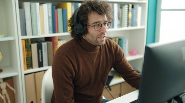 Young hispanic man student using computer and headphones studying at library university