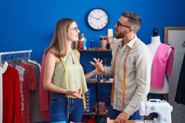 Man and woman tailors smiling confident speaking at clothing factory