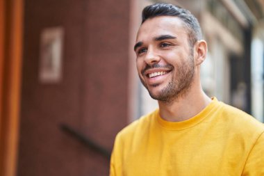 Young hispanic man smiling confident looking to the side at street