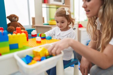 Teacher and toddler playing with construction blocks sitting on table at kindergarten