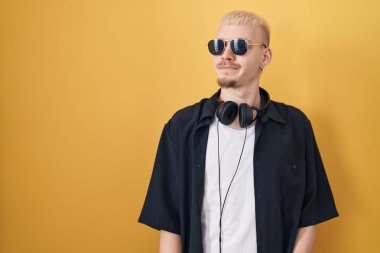 Sarı arka planda duran güneş gözlüklü genç, beyaz bir adam gülümsüyor ve diğer tarafa bakıyor.. 