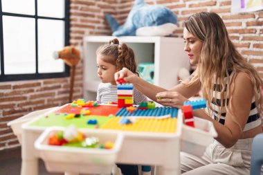 Teacher and toddler playing with construction blocks sitting on table at kindergarten