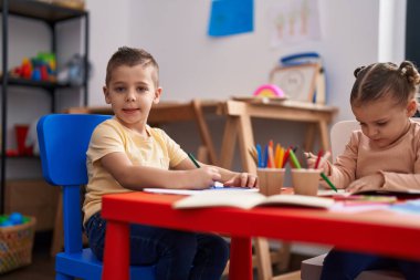 Two kids preschool students sitting on table drawing on paper at kindergarten