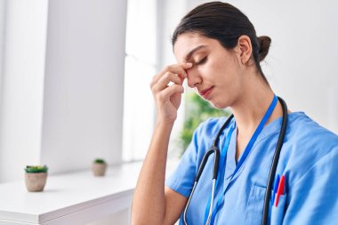 Young beautiful hispanic woman doctor stressed standing at clinic