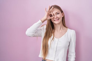 Pembe arka planda dikilen beyaz bir kadın el hareketleriyle gülümsüyor ve mutlu yüzüyle parmaklarının arasından bakıyor.. 