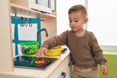 Adorable hispanic boy playing with play kitchen standing at kindergarten