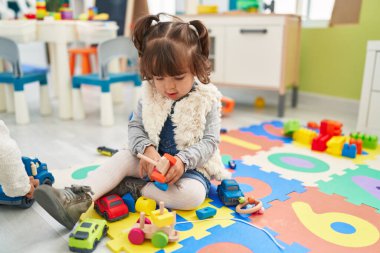 Adorable hispanic toddler playing with car toy sitting on floor at kindergarten