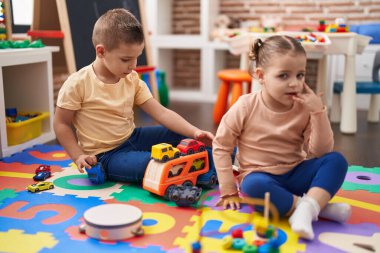Two kids playing with cars toy sitting on floor at kindergarten