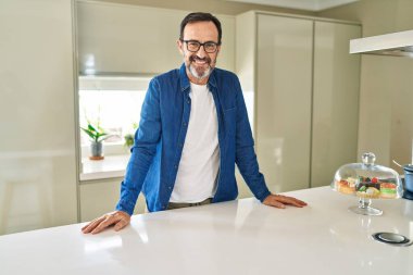 Orta yaşlı bir adam evde kendine güvenerek gülümsüyor.