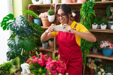 Young beautiful arab woman florist make photo to flowers by smartphone at flower shop