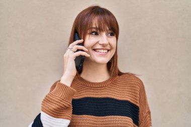 Gülümseyen genç bir kadın caddedeki akıllı telefondan konuşuyor.