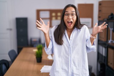 Ofisteki genç İspanyol kadın başarı için kızgın ve çılgınlığı kutluyor kollarını kaldırmış ve gözlerini kapatmış heyecanla bağırıyor. Kazanan konsept 