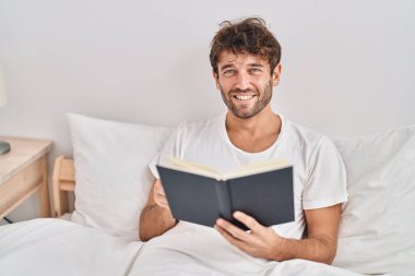 Yatak odasında kitap okuyan genç bir adam.
