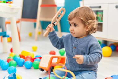 Sevimli İspanyol bebek elinde oyuncakla anaokulunda yerde oturuyor.