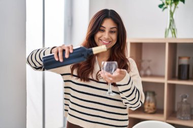 Young hispanic woman smiling confident pouring wine on glass at home