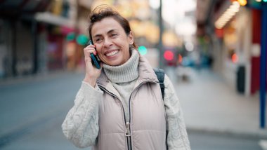 Orta yaşlı İspanyol kadın gülümsüyor. Akıllı telefondan konuşuyor.