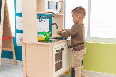 Adorable hispanic boy playing with play kitchen standing at kindergarten