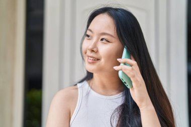 Genç Çinli kadın gülümsüyor caddede akıllı telefondan konuşuyor.