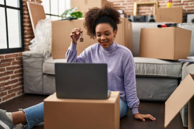 Young african american woman showing keys of new home on video call looking positive and happy standing and smiling with a confident smile showing teeth 