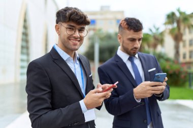 İki İspanyol işadamı sokakta akıllı telefon kullanarak gülümsüyor.