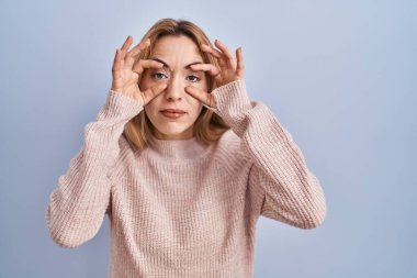 Mavi arka planda dikilen İspanyol kadın parmaklarıyla gözlerini açmaya çalışıyor, uykulu ve yorgun sabah yorgunluğu için. 