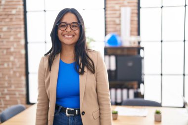 Brunette woman working at the office wearing glasses looking positive and happy standing and smiling with a confident smile showing teeth 