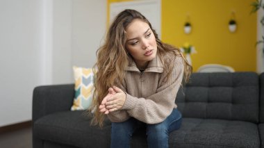 Young beautiful hispanic woman sitting on sofa with serious expression at home