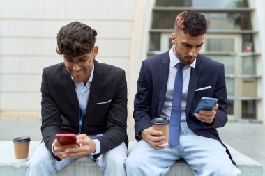 Two hispanic men business workers using smartphones drinking coffee at street