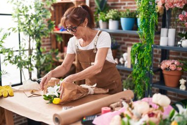 Middle age woman florist make bouquet of flowers at flower shop