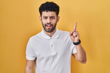Arab man standing over yellow background pointing finger up with successful idea. exited and happy. number one. 