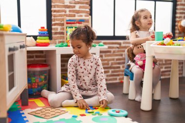 İki çocuk anaokulunda yerde oturmuş bulmaca oynuyorlar.