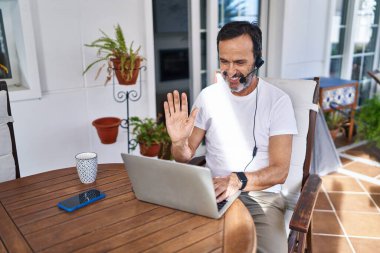 Middle age man wearing call center agent headset working from home looking positive and happy standing and smiling with a confident smile showing teeth 