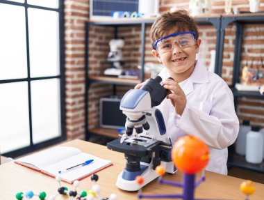 Adorable hispanic boy student smiling confident using microscope at laboratory classroom