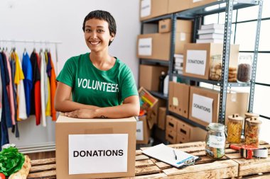 Hayır kurumunda bağış paketine yaslanmış gönüllü üniforması giyen İspanyol genç bir kadın.