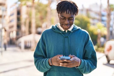 Sokakta akıllı telefon kullanan, kendinden emin gülümseyen Afrikalı Amerikalı bir adam.