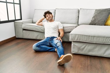 Genç İspanyol adam evde müzik dinlerken kendinden emin gülümsüyor.