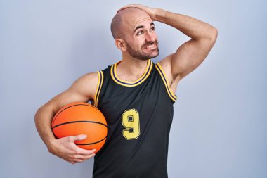 Sakallı, basketbol forması giyen, top tutan, kendine güvenen, saçlara dokunan, el hareketi yapan çekici ve şık görünümlü kel bir adam. 