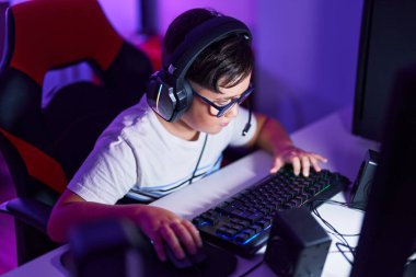 Adorable hispanic boy streamer playing video game using computer at gaming room