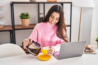 Young hispanic woman having breakfast using laptop at home
