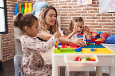 Teacher with girls playing with construction blocks sitting on table at kindergarten