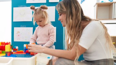 Teacher and toddler playing with construction blocks sitting on table at kindergarten