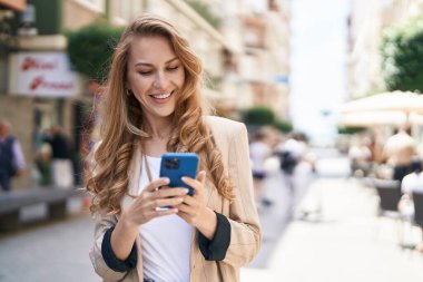 Sokakta akıllı telefon kullanan, kendine güvenen genç sarışın kadın.