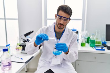 Laboratuvarda test tüpüne sıvı döken bilim adamı üniforması giyen İspanyol genç adam.